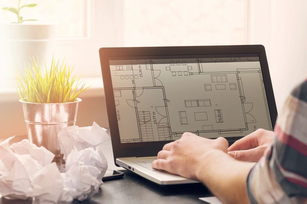 Architect reviewing floor plans on a laptop for space planning and furniture layout